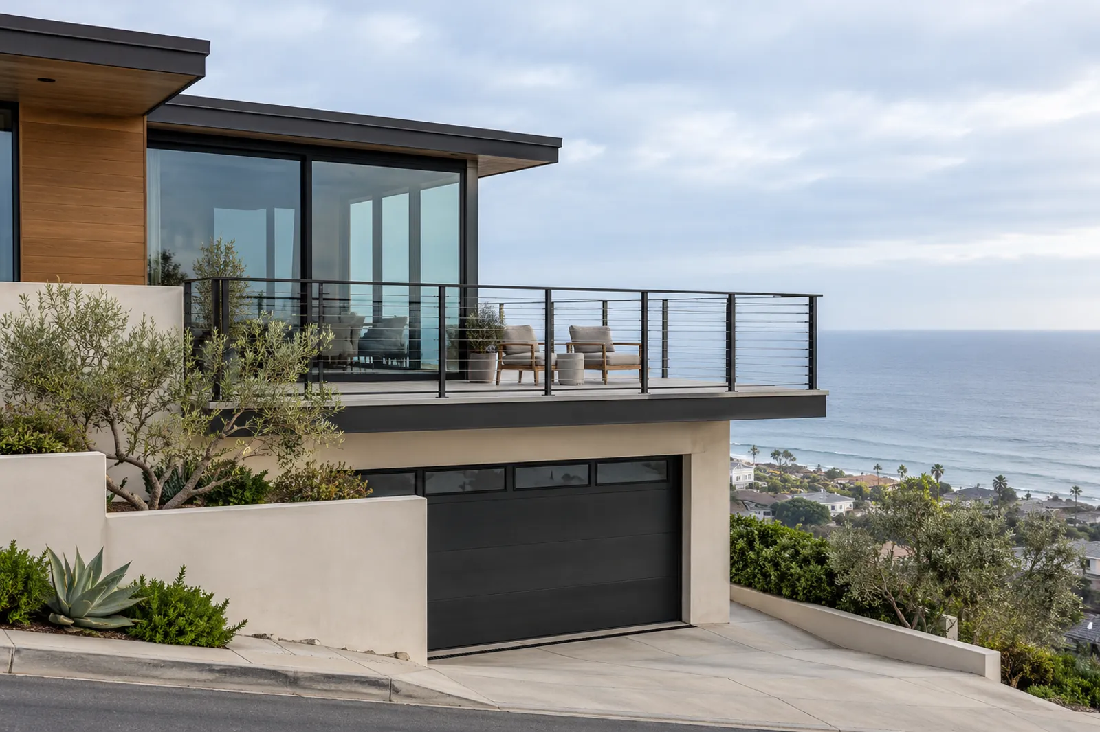 Horizontal stainless cable railing on dark steel posts along an upper deck facing the ocean, two outdoor chairs