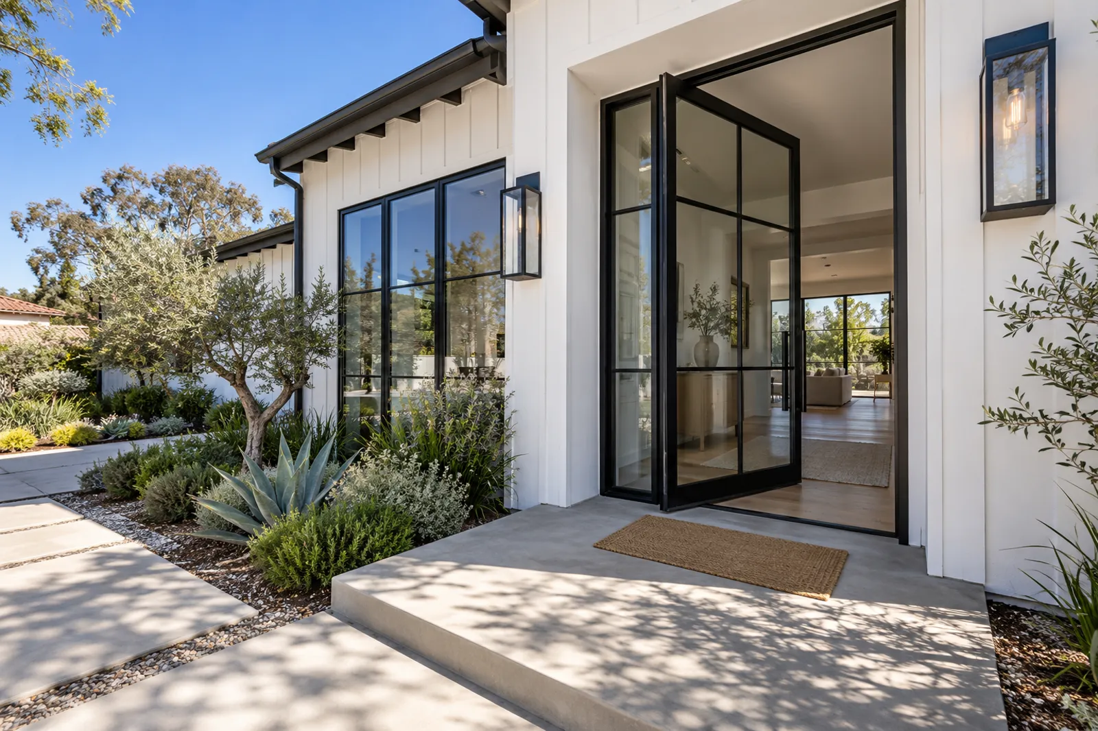 Tall black steel and glass pivot entry door standing open on a white board-and-batten modern farmhouse